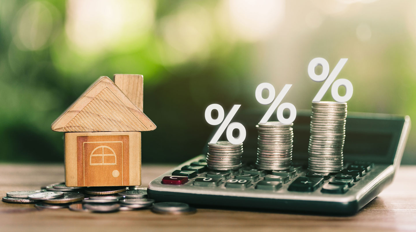 Main de professionnel complétant au stylo un tableau de plan de financement multi-sources avec colonnes PTZ 2026, Action Logement, Prêt principal et Apport personnel, sur un bureau de courtier avec calculatrice et documents en arrière-plan
